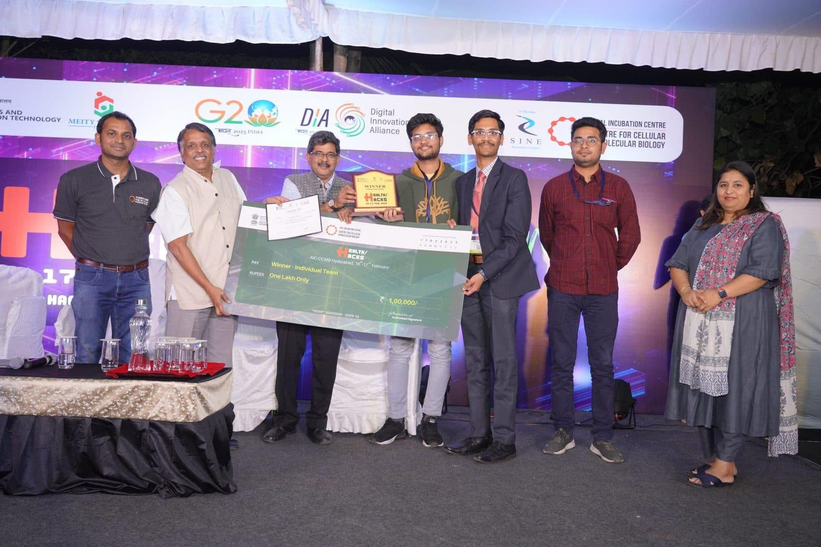 Winning team on stage holding a trophy and a large presentation cheque