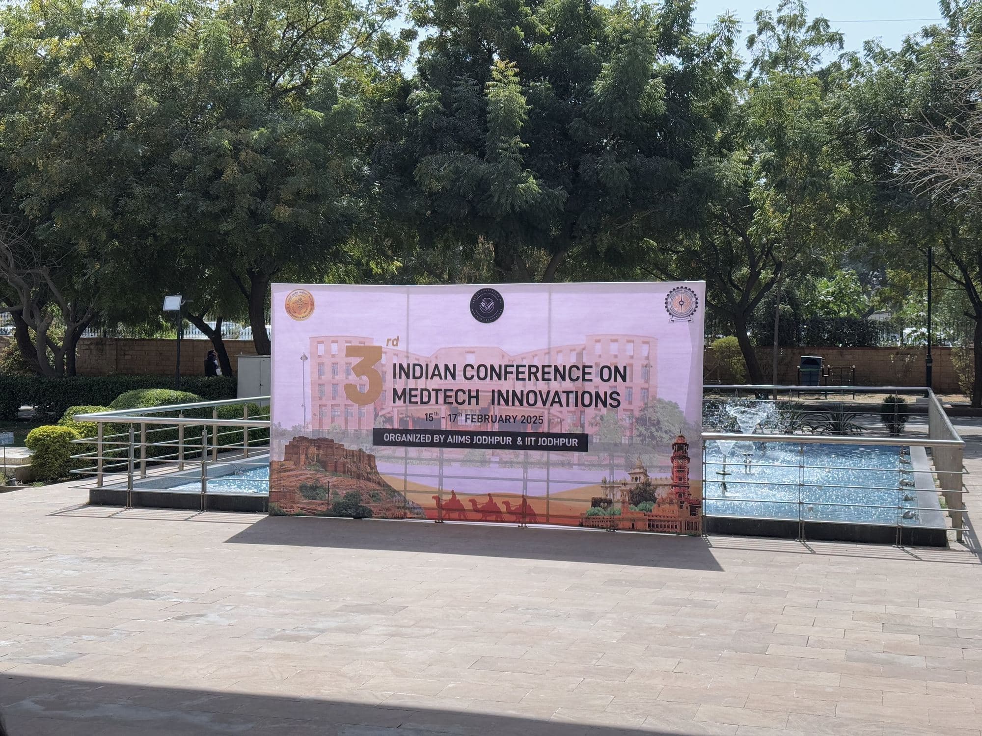 Indian Conference on MedTech Innovations banner beside a fountain, framed by trees