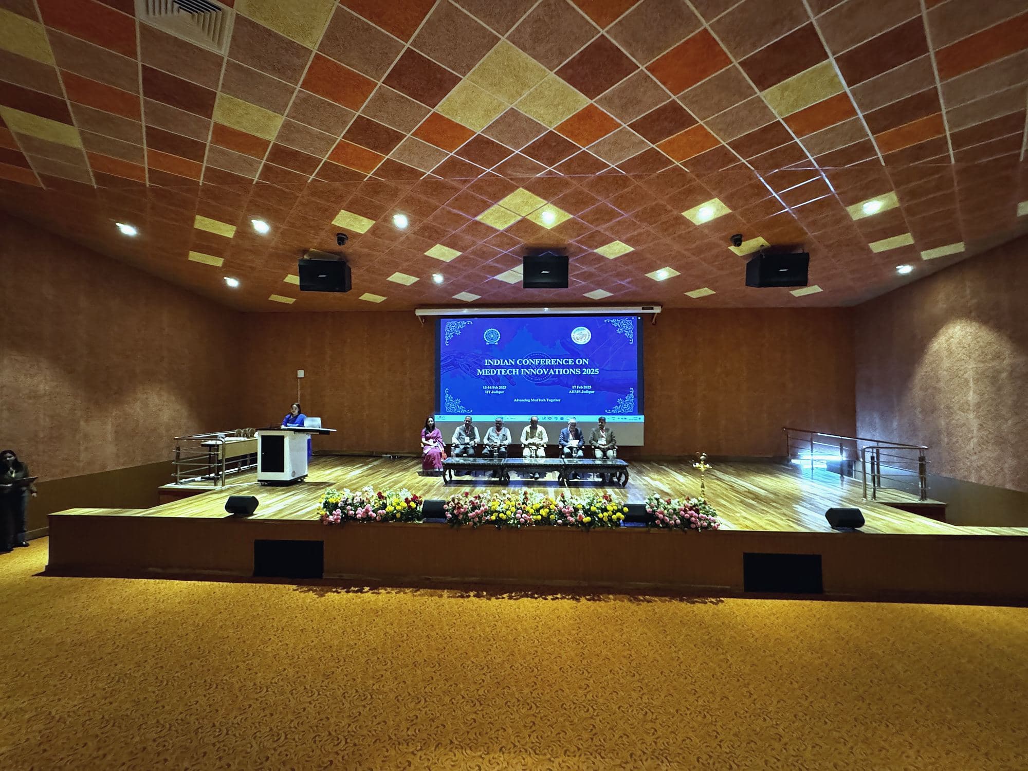 Wide view of the auditorium stage with the ICMI title on the screen and panel seated