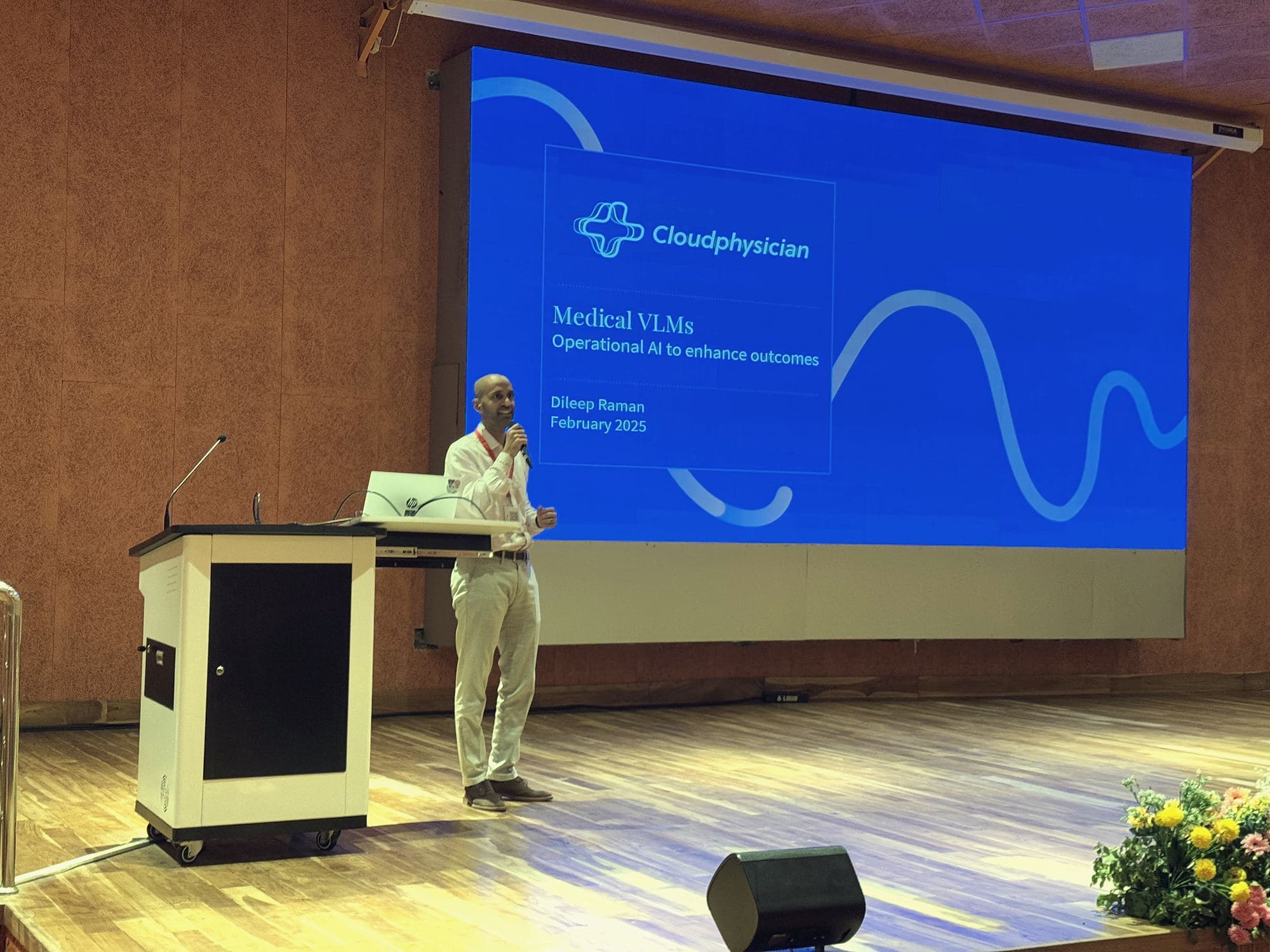 Speaker at the podium presenting on medical AI in front of a large screen