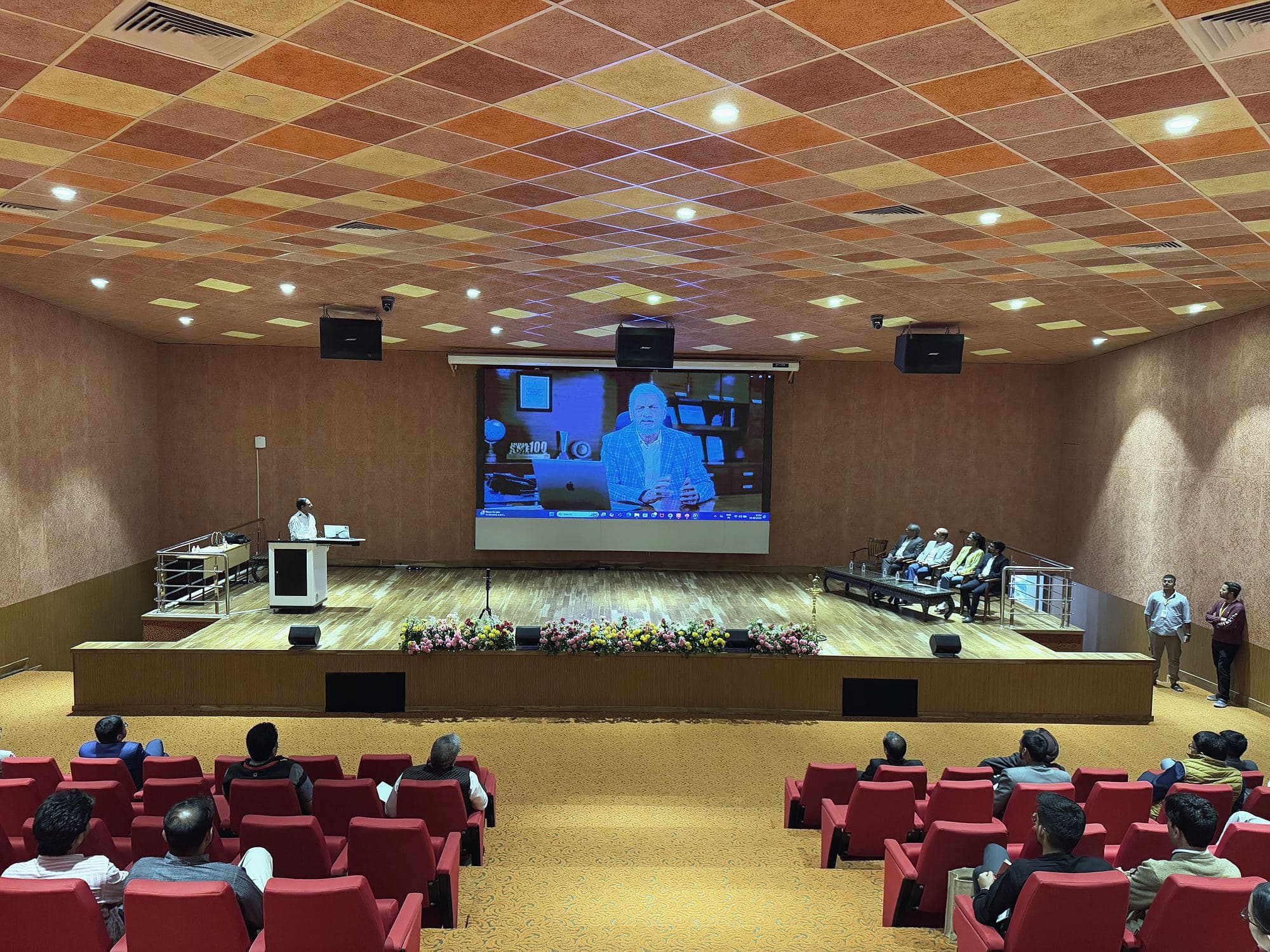 Audience in the auditorium watching a speaker shown on the big screen