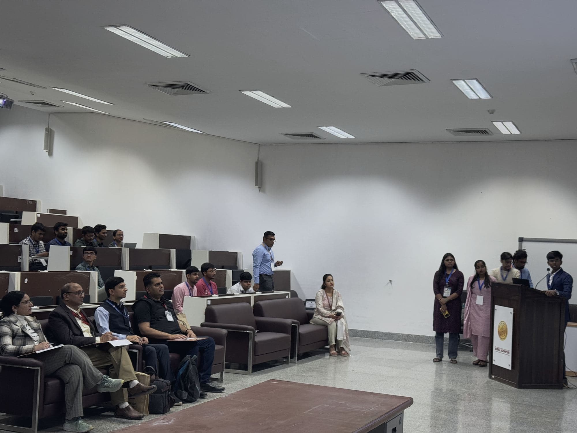 Presenter at a lectern addressing a seated audience in a lecture hall